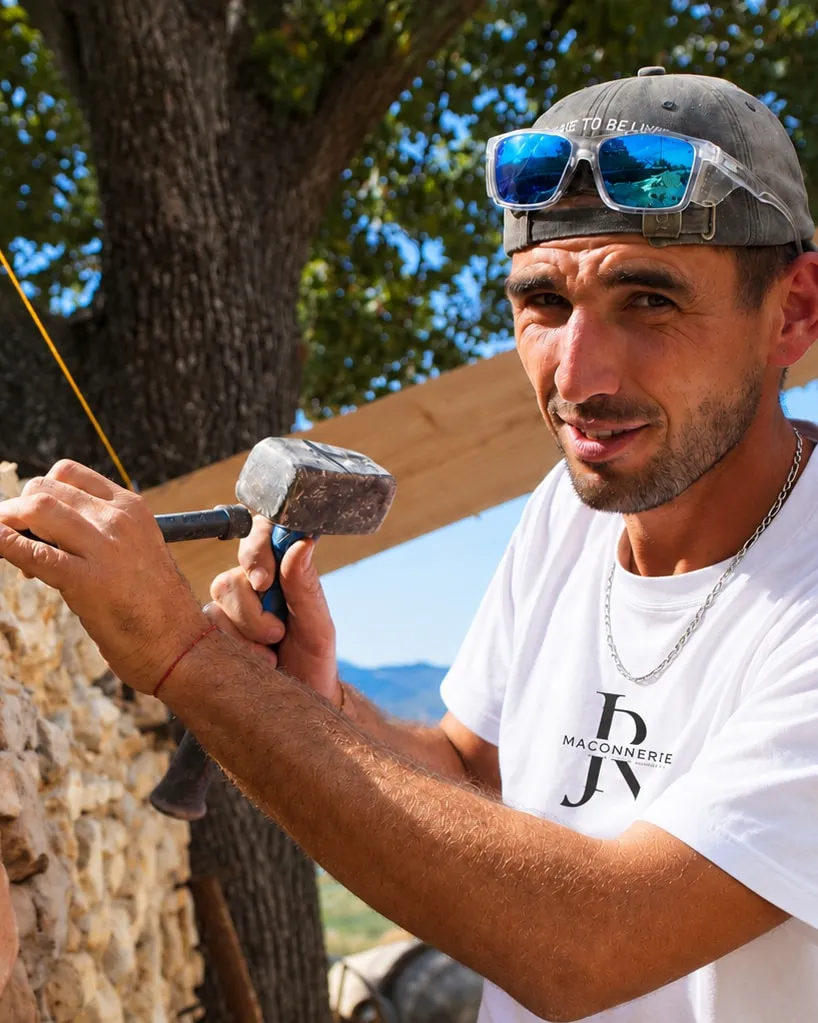 Jérémy Rochas, gérant de JR MACONNERIE RENOVATION, massette et ciseau en main devant un mur en pierre